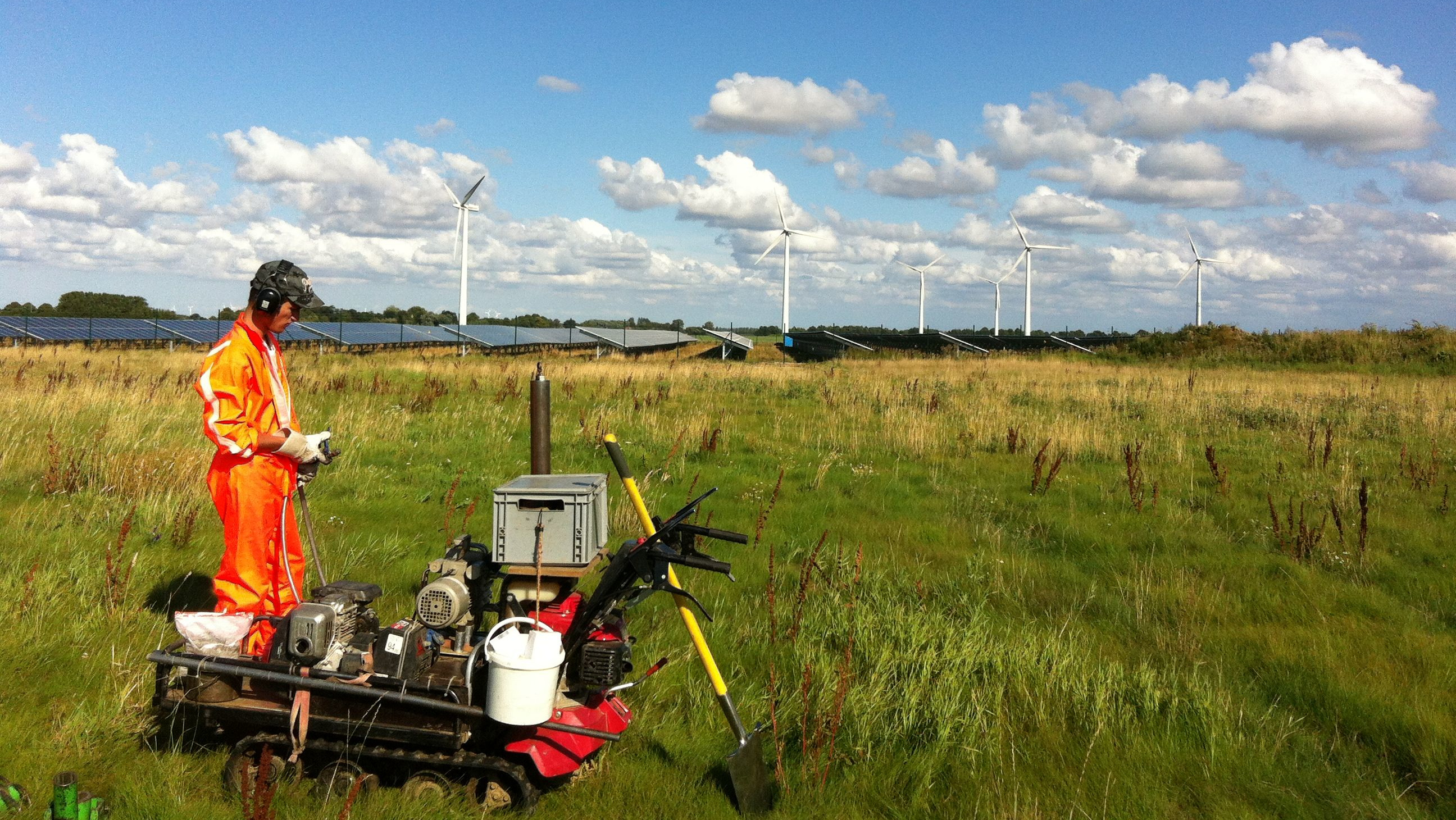 Geotechniker bei der Feldarbeit, im Hintergrund eine PV-Anlage und Windkraftanlagen